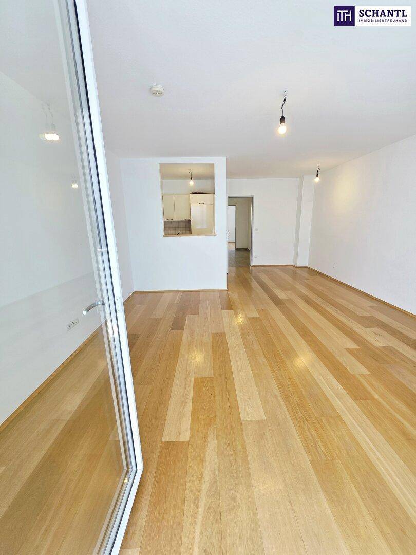 Geräumiges Wohnzimmer mit hellem Holzboden und offener Verbindung zur Küchennische.