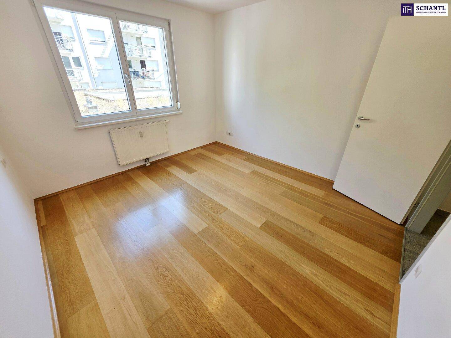 Schlafzimmer mit Holzboden und Blick auf die umliegenden Gebäude, bietet viel Tageslicht.