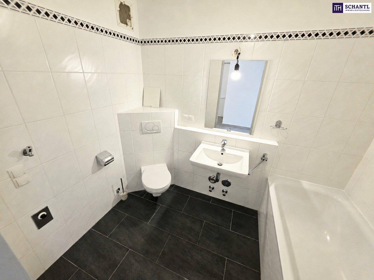 Badezimmer mit Badewanne, WC, Waschbecken und dunklen Bodenfliesen, in gutem Zustand.