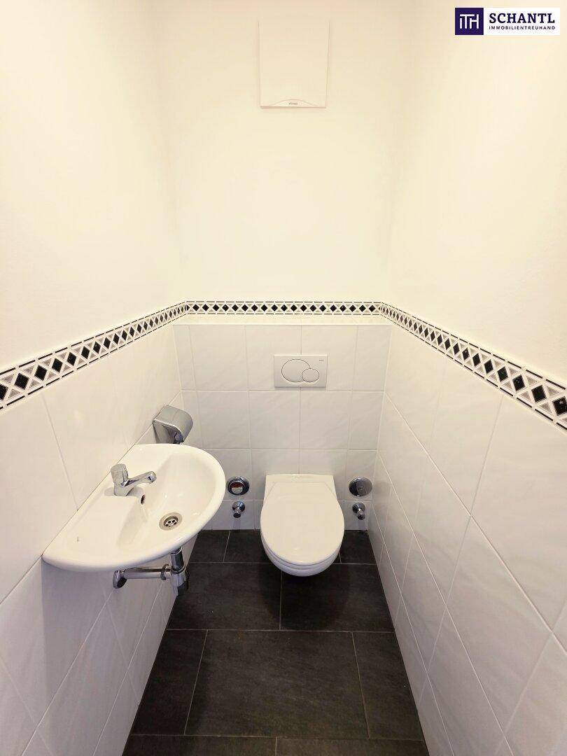 Separates WC mit Waschbecken und dunklem Fliesenboden, sauber und funktional.