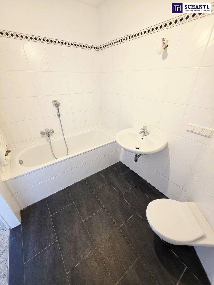 Badezimmer mit Badewanne, Waschbecken und WC, ausgestattet mit weißen und dunklen Fliesen.