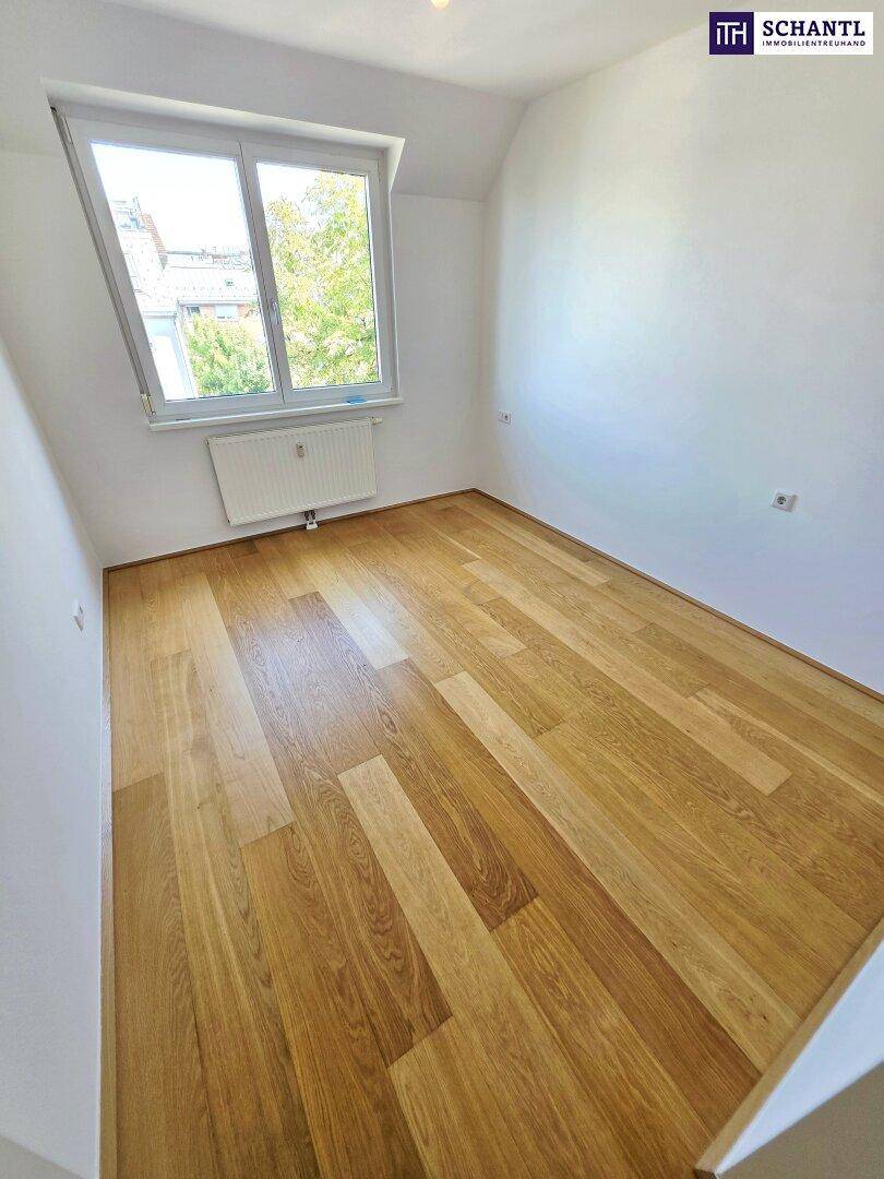 Helles Zimmer mit Holzparkettboden, Dachschräge und Fenster mit Blick ins Grüne.