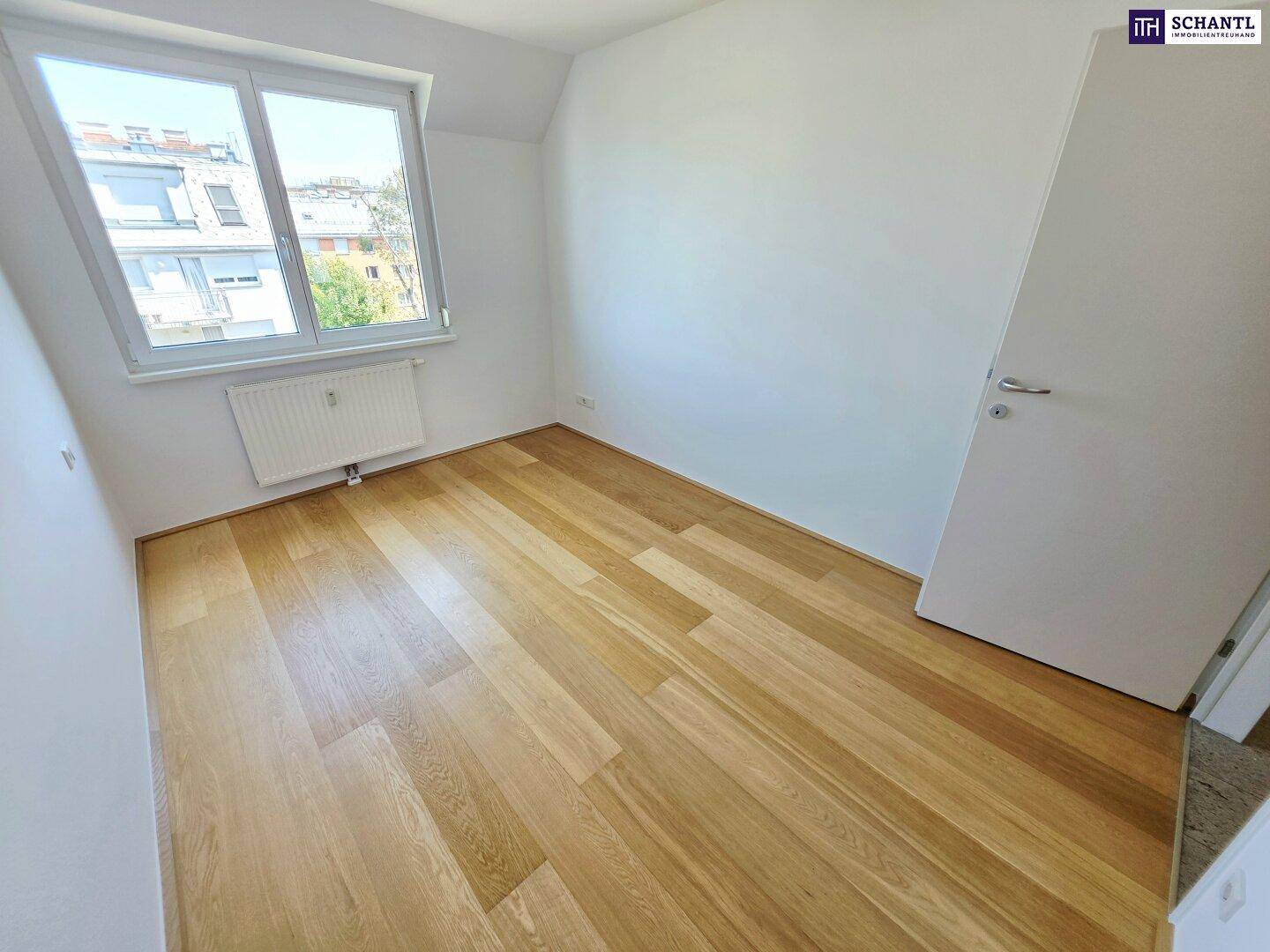 Helles Zimmer mit Holzparkettboden und Fenster, das viel Tageslicht bietet.