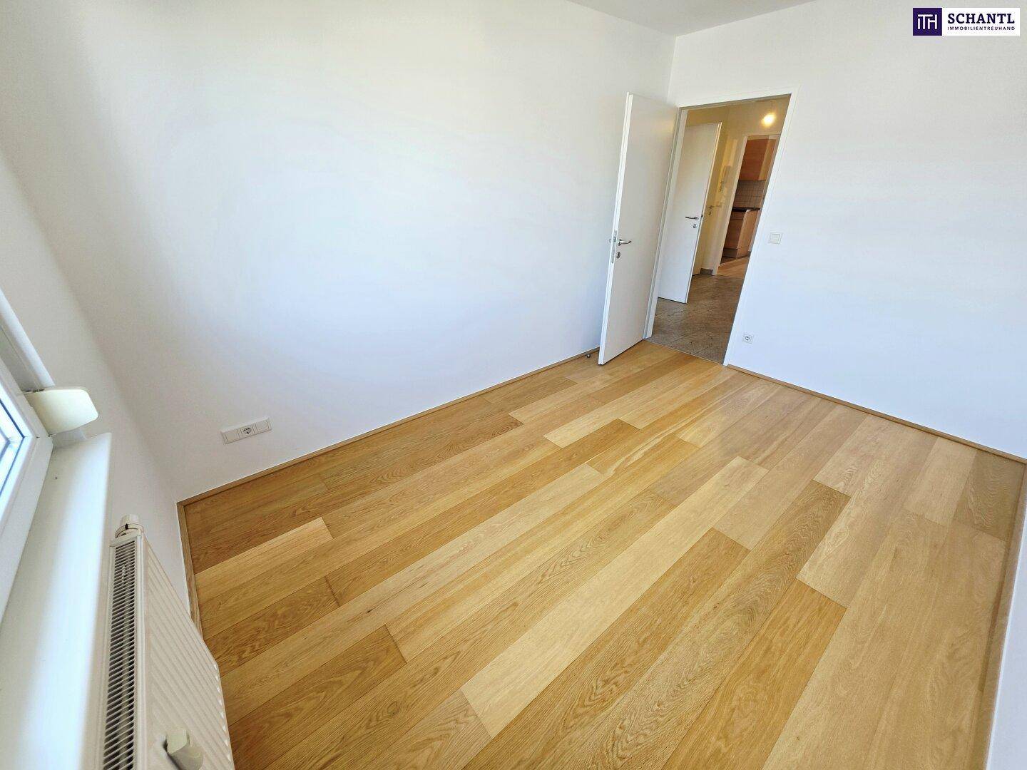 Geräumiges Zimmer mit hellem Holzparkett und einem Fenster, das viel Tageslicht hereinlässt.