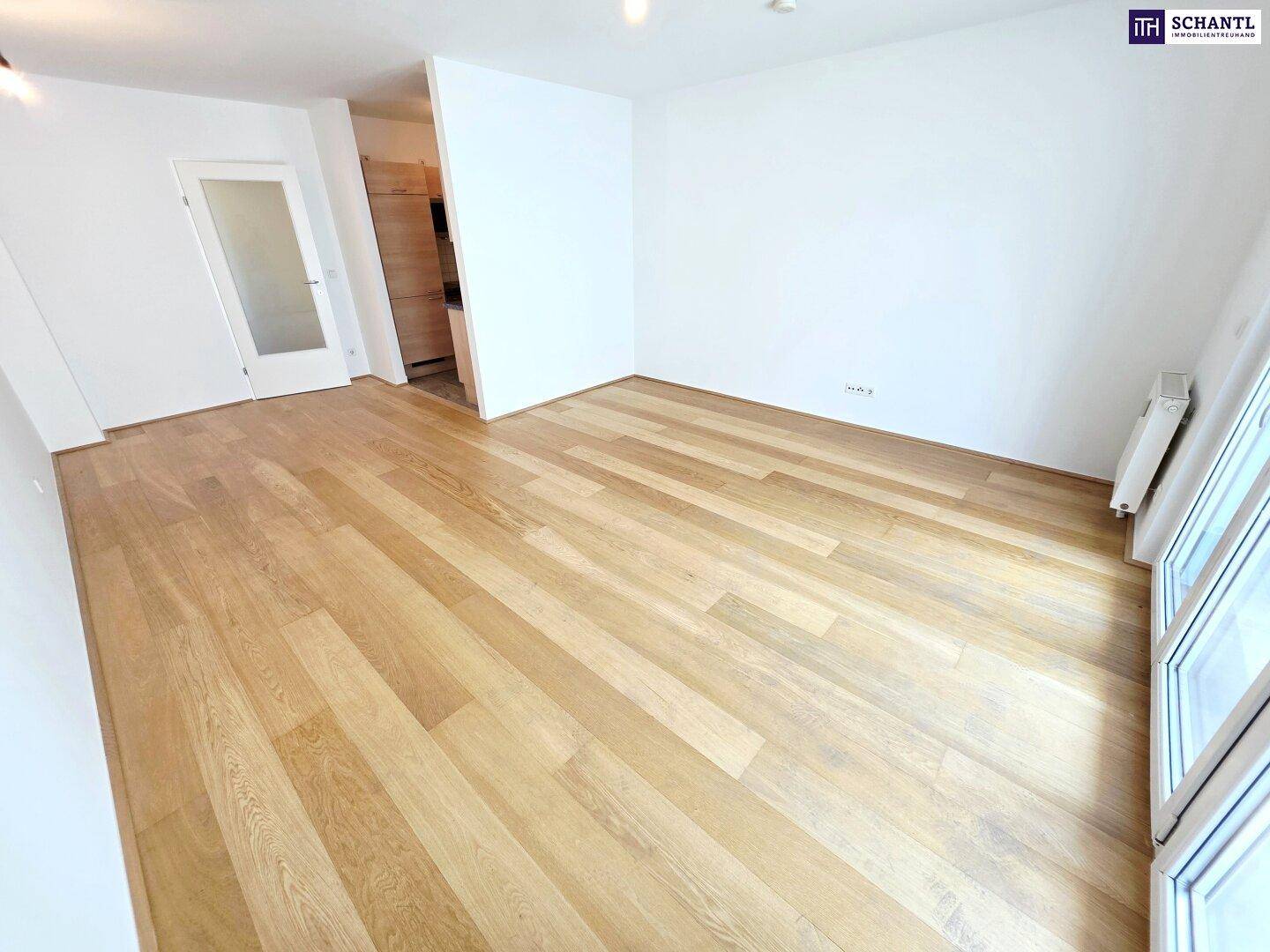 Heller, leerer Wohnbereich mit Holzparkettboden und Zugang zu einem weiteren Zimmer.
