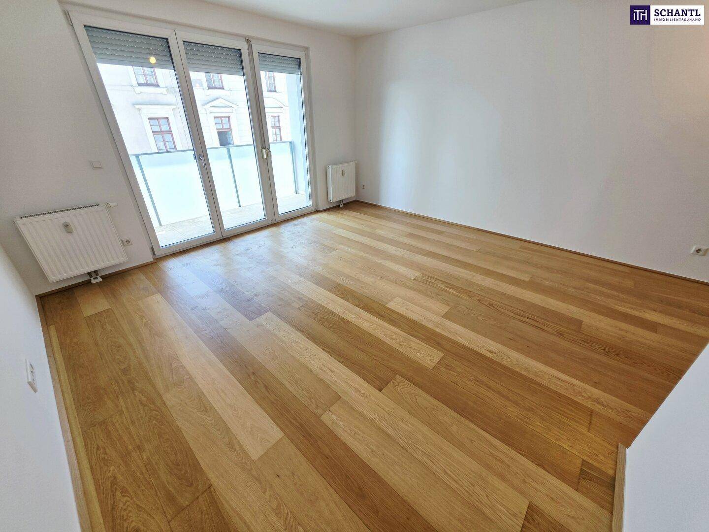 Lichtdurchfluteter Raum mit Holzparkettboden und großen Fenstern, die Zugang zum Balkon bieten.
