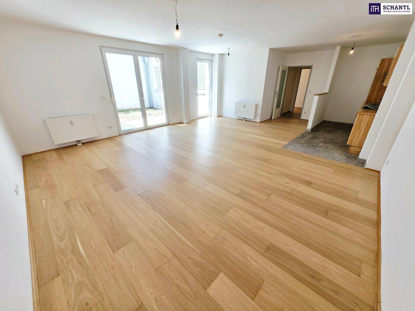 Heller Wohnbereich mit Holzboden und großen Fenstern, die Zugang zum Außenbereich bieten.