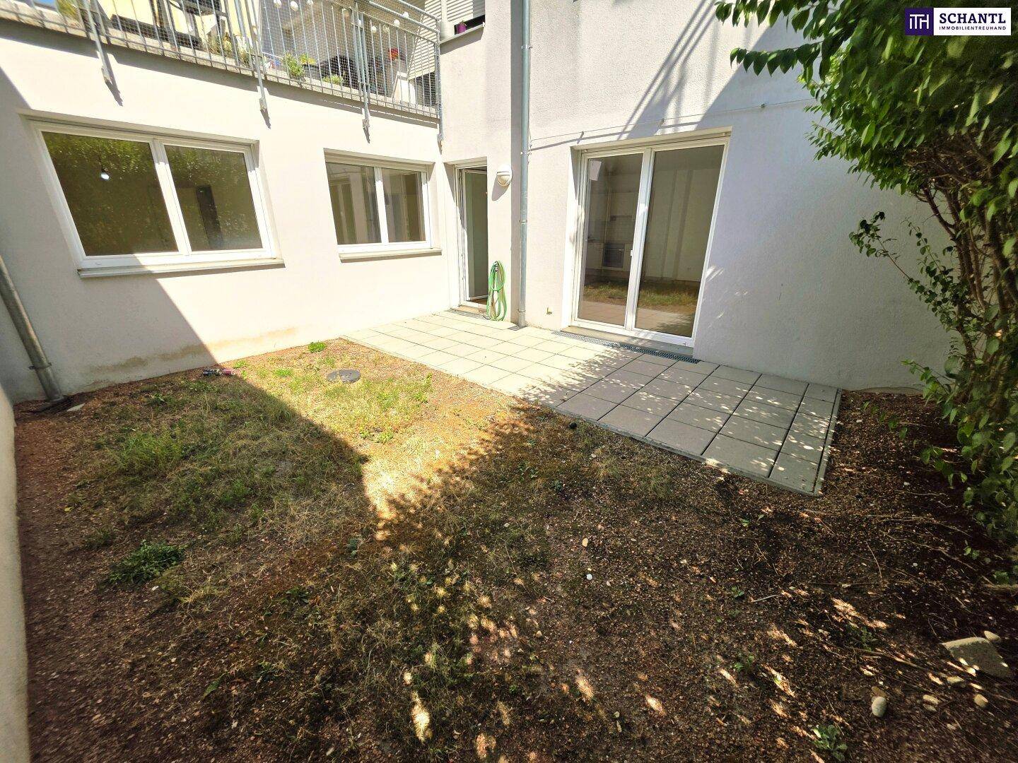 Kleiner Gartenbereich mit gepflasterter Terrasse und Rasenfläche hinter dem Gebäude.