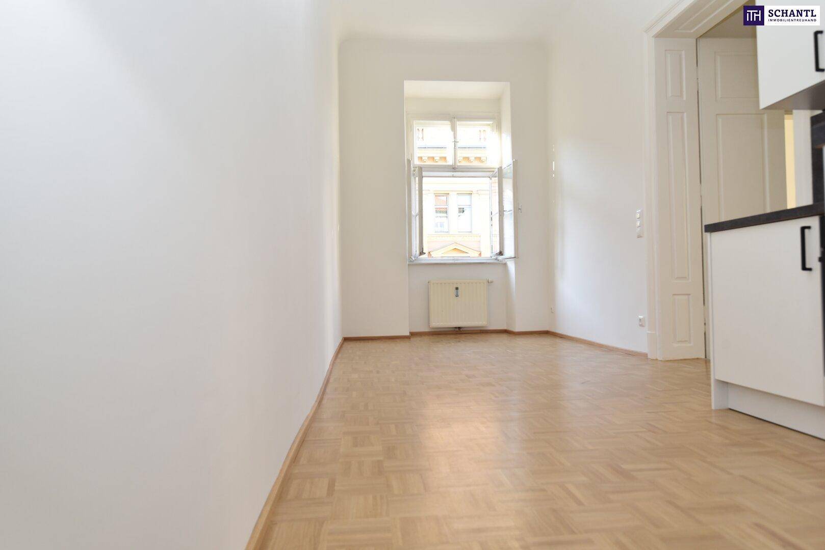Heller Raum mit Parkettboden und Fenster, angrenzend an eine moderne Küchenzeile.