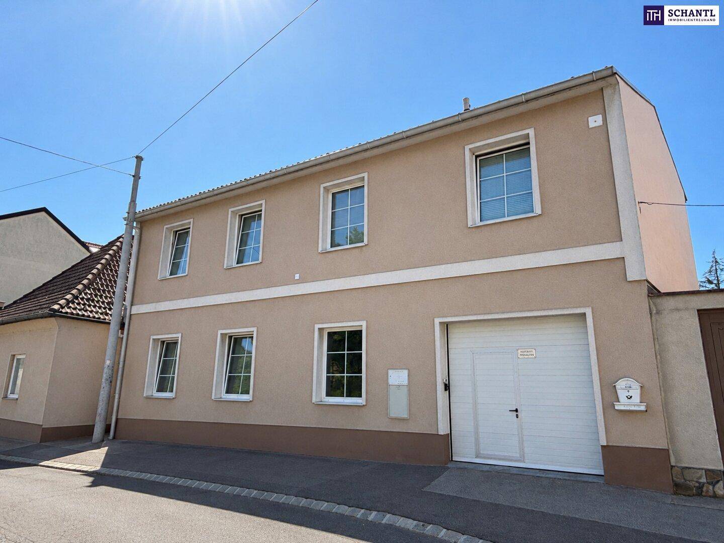 Gesamtansicht der Hausfassade von der Straße mit Garage und Fenstern unter blauem Himmel.