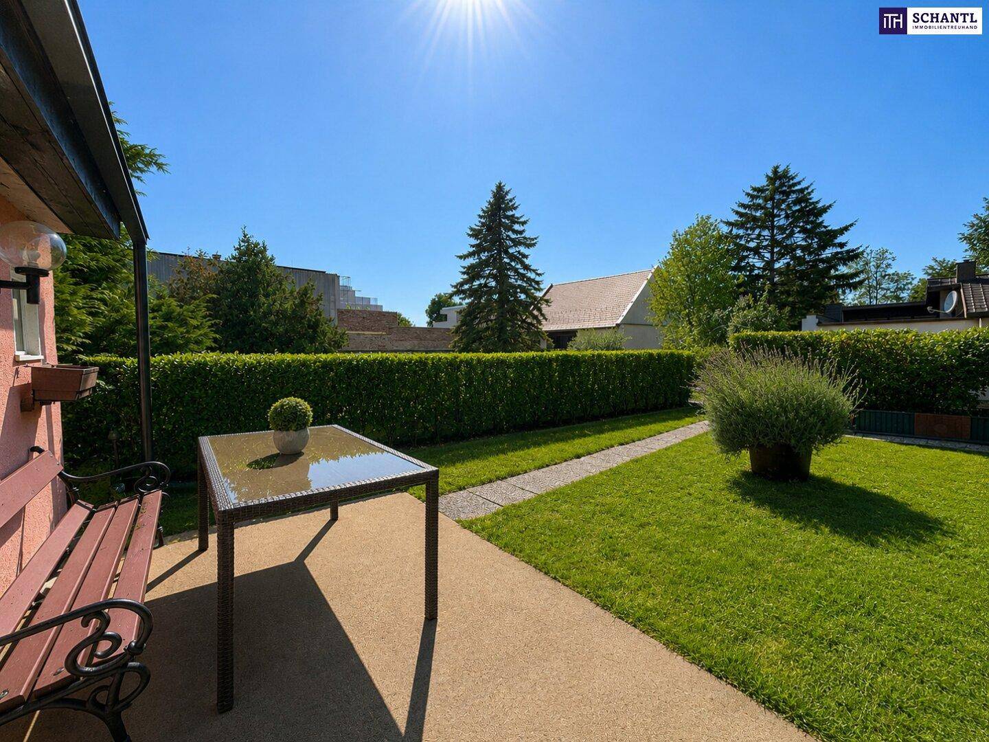Gemütliche Terrasse mit Gartentisch und Bank, umgeben von Grünflächen und Hecken.