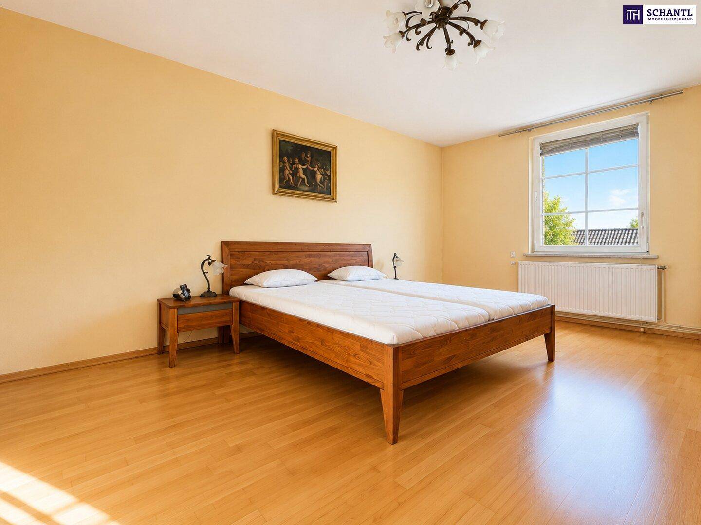 Schlafzimmer mit Holzbett, Nachttischen und hellem Laminatboden, gut beleuchtet durch ein Fenster.