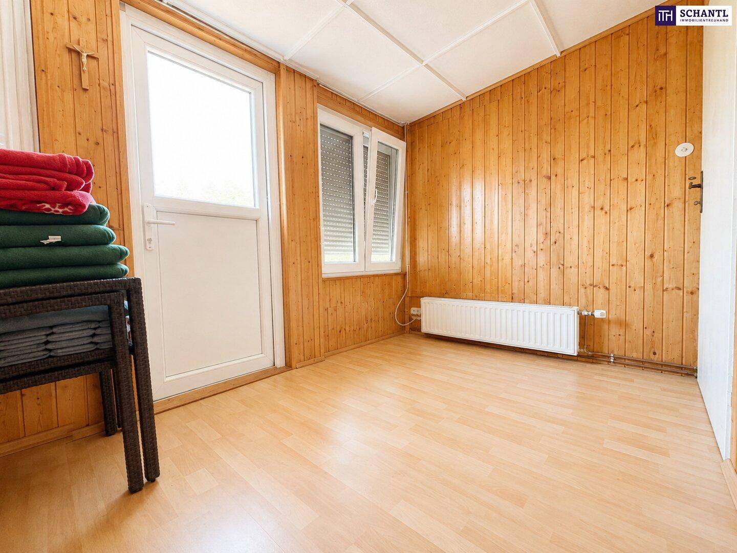 Heller Raum mit Holzvertäfelung an Wänden und Decke, Laminatboden und Zugang nach draußen.