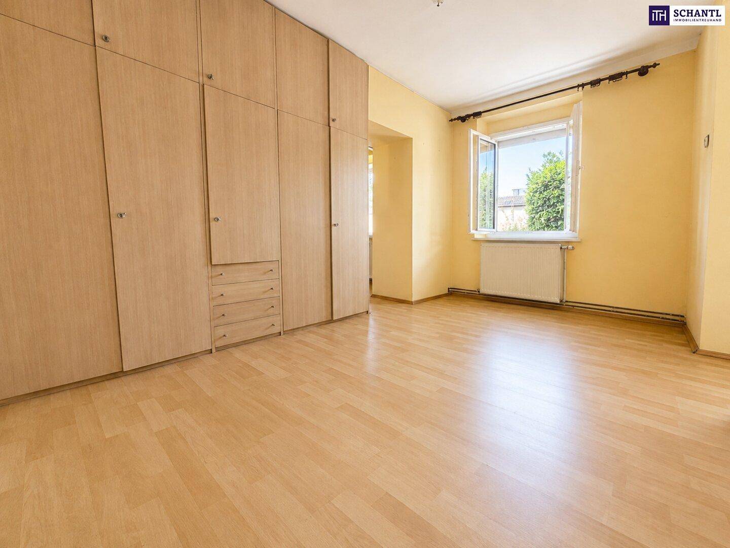Schlafzimmer mit großem Einbauschrank, Laminatboden und Fenster, das Tageslicht hereinlässt.