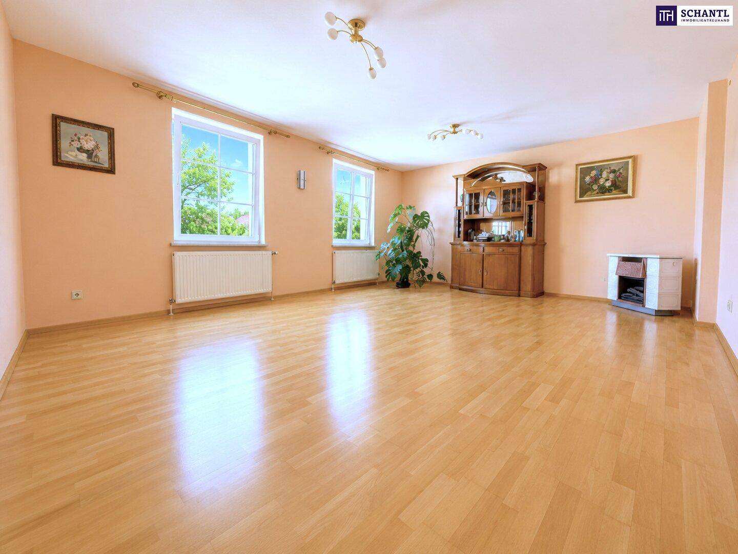 Helles Wohnzimmer mit hellem Laminatboden, großen Fenstern und traditionellen Möbeln.
