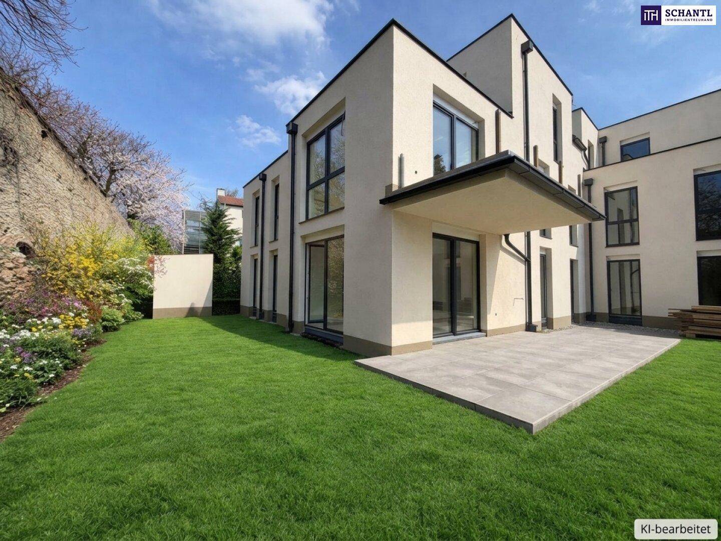 Neubau mit großer gepflasterter Terrasse und privatem Gartenbereich neben einer alten Steinmauer.