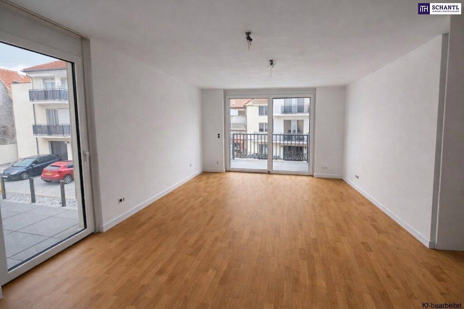 Helles, leeres Wohnzimmer mit Holzboden, großen Fenstern und Zugang zum Balkon.