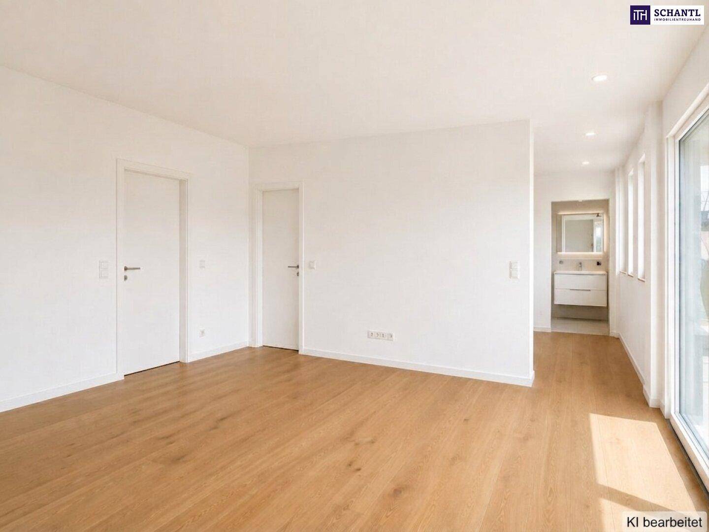Heller, leerer Raum mit Holzboden und Blick in ein modernes Badezimmer.