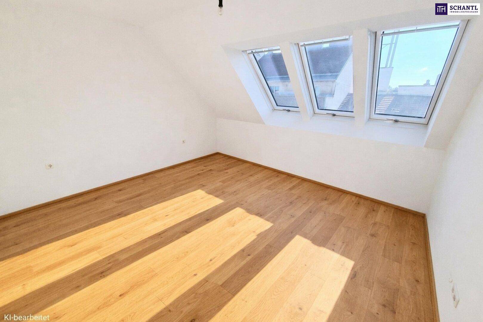 Helles Dachzimmer mit schrägen Wänden, Holzfußboden und drei großen Dachfenstern für viel Tageslicht.