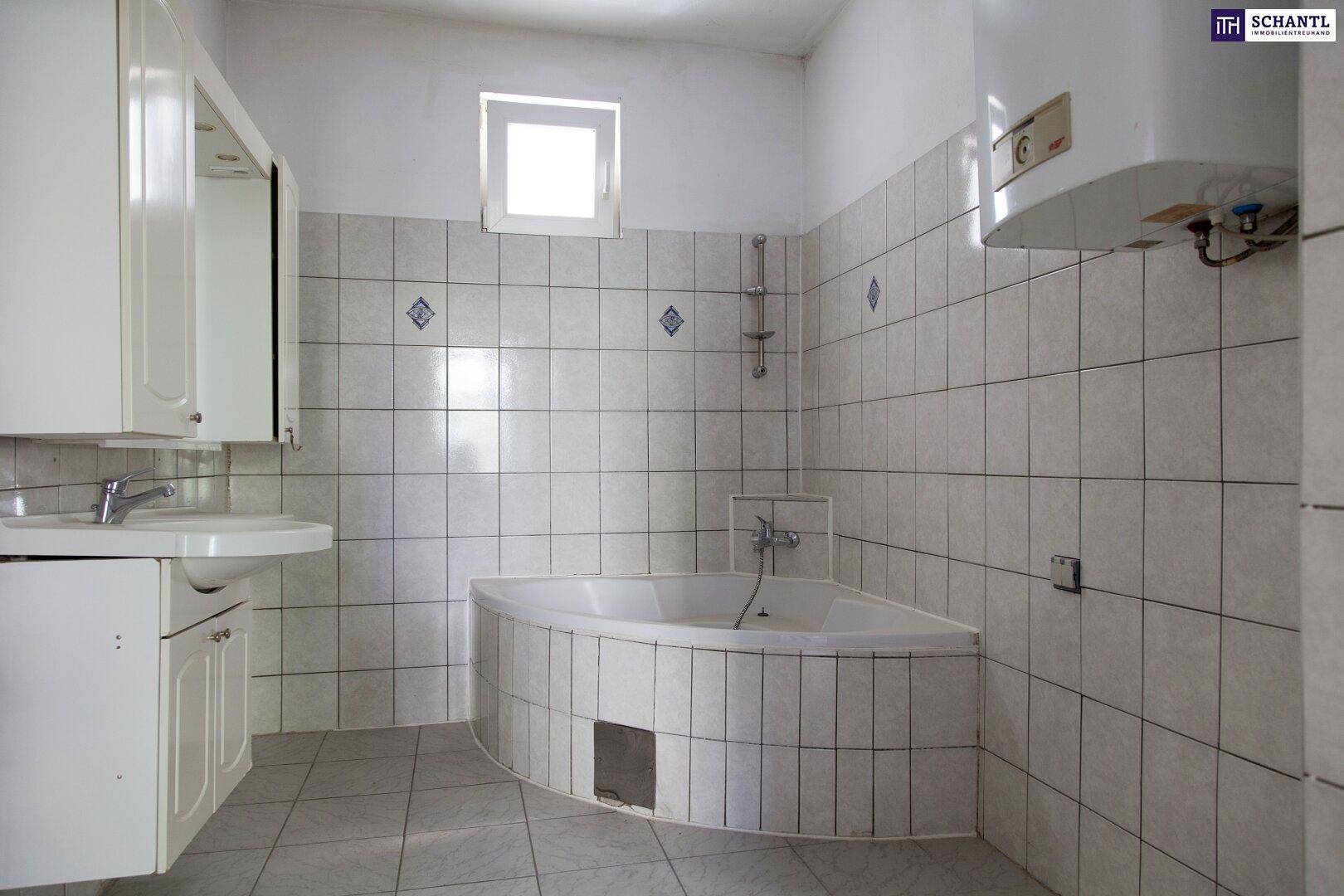 Badezimmer mit Eckbadewanne, weißen Fliesen, Waschbecken und Fenster.