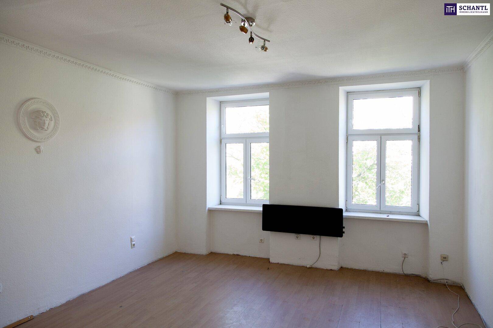 Heller Raum mit zwei Fenstern, Holzboden und dekorativer Deckenleiste.