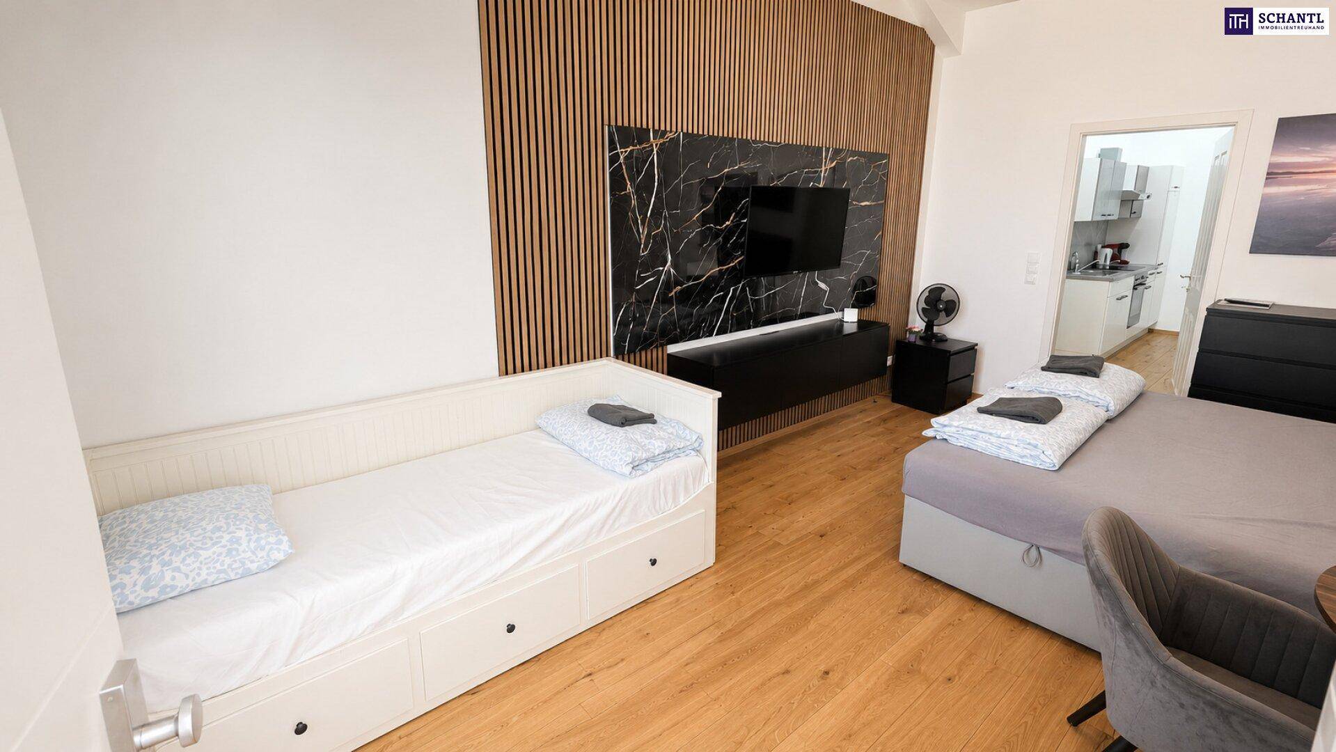 Helles Schlafzimmer mit Holzboden, einem Einzelbett und einem modernen TV-Bereich mit dunkler Marmoroptik.