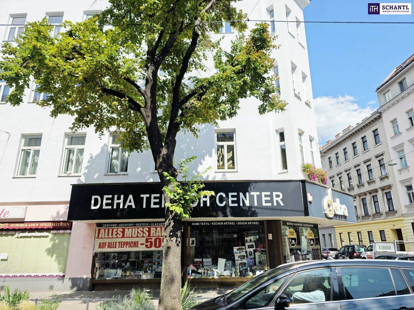 Gebäudefassade mit einem Teppichgeschäft im Erdgeschoss und Bäumen davor.