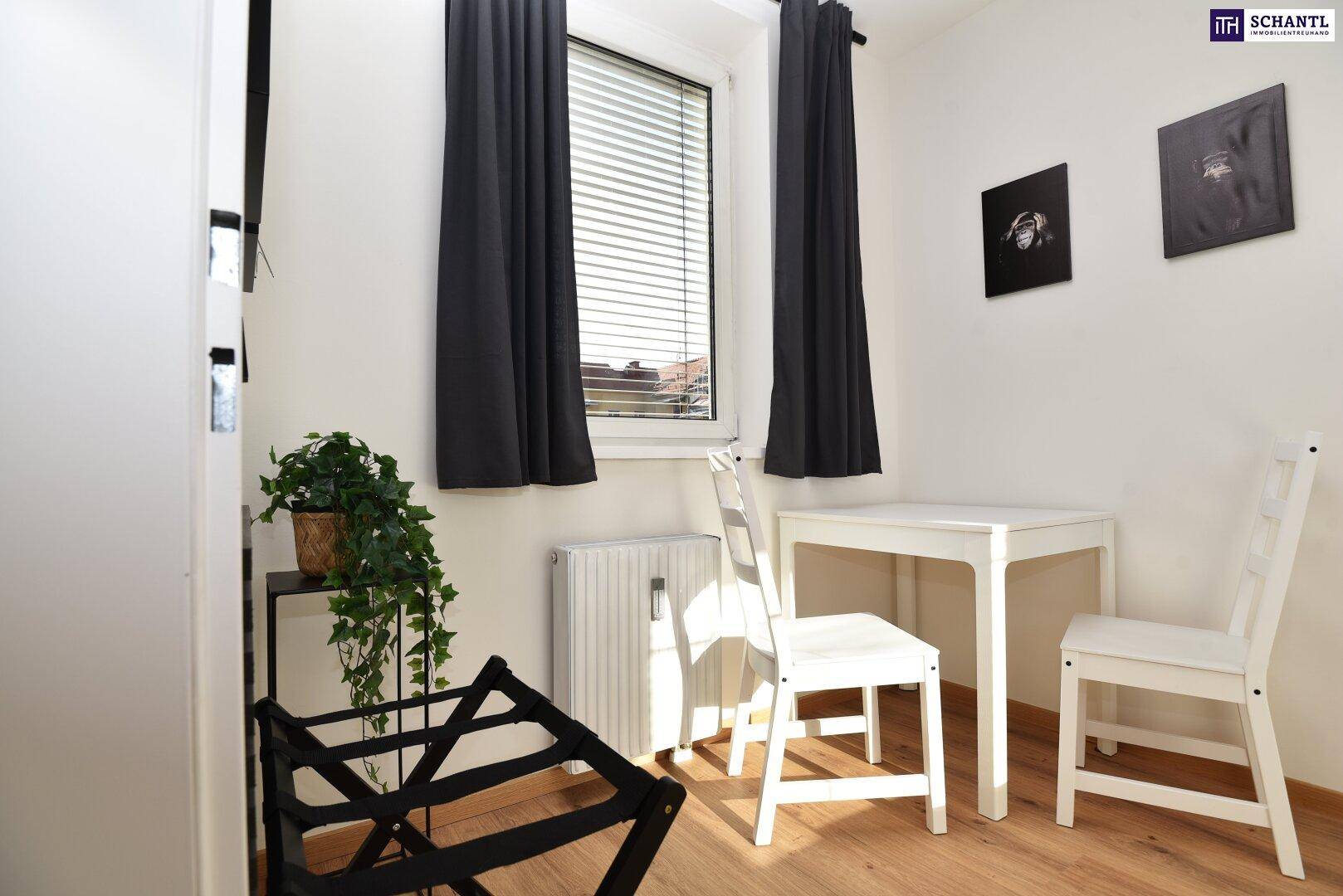 Kleiner Essbereich mit weißem Tisch und Stühlen, Holzboden und einem Fenster mit Jalousien.