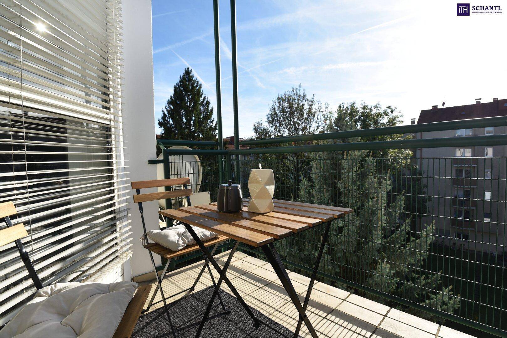 Heller Balkon mit Holztisch und Stühlen, umgeben von Bäumen und mit Blick ins Grüne.