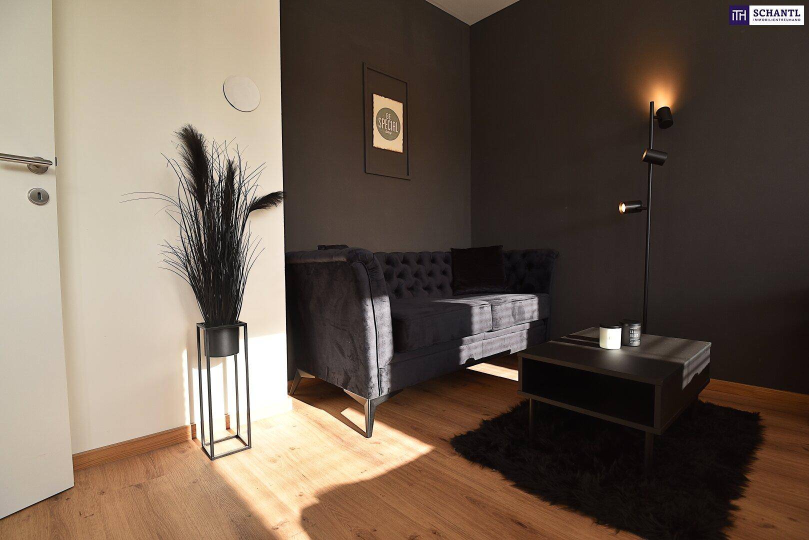 Gemütliche Sitzecke mit dunklem Sofa, Couchtisch und einer modernen Stehlampe auf Holzboden.