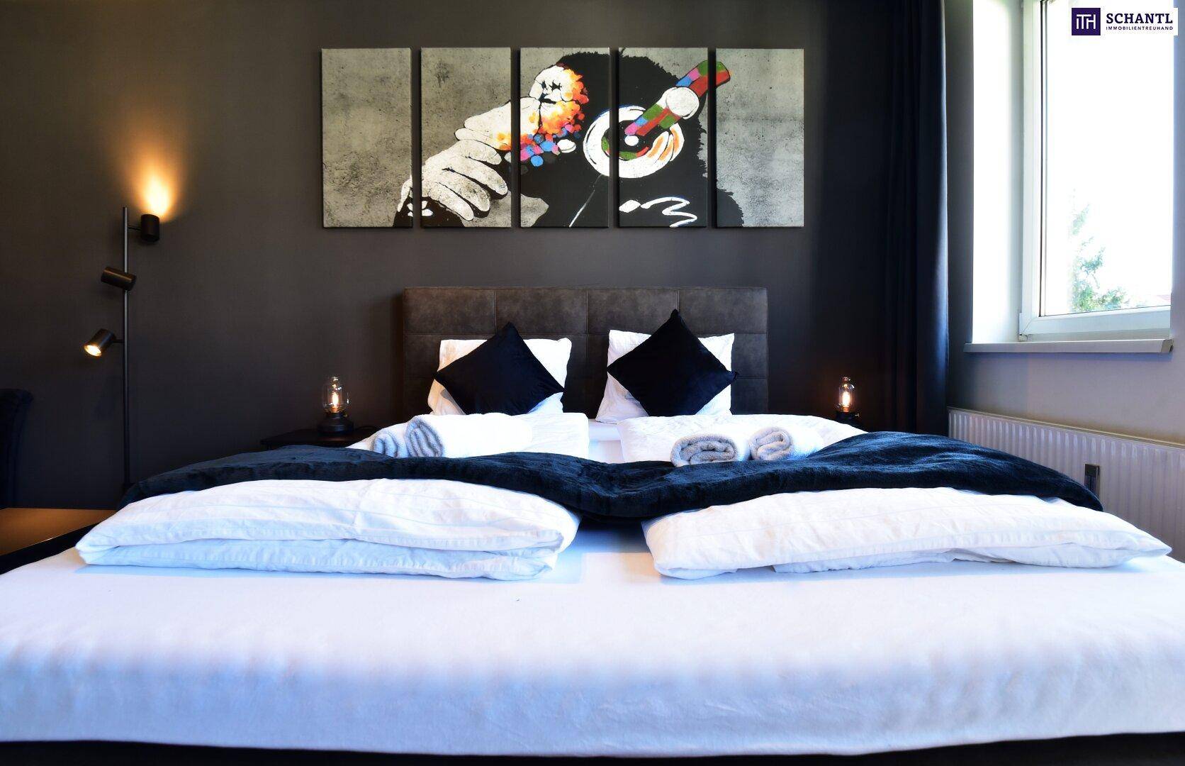 Schlafzimmer mit großem Bett, dunklen Wänden und einem Fenster, das Tageslicht hereinlässt.