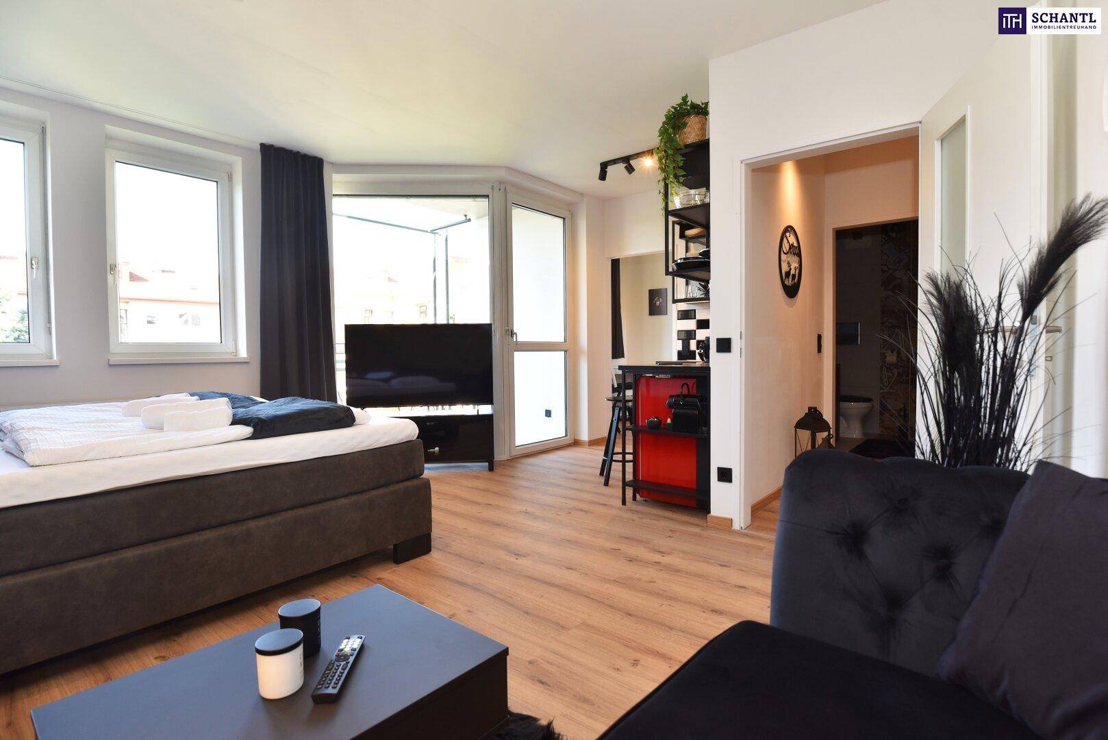 Offener Wohn- und Essbereich mit Bett, Sofa, Küchenzeile und Zugang zu einem Balkon.