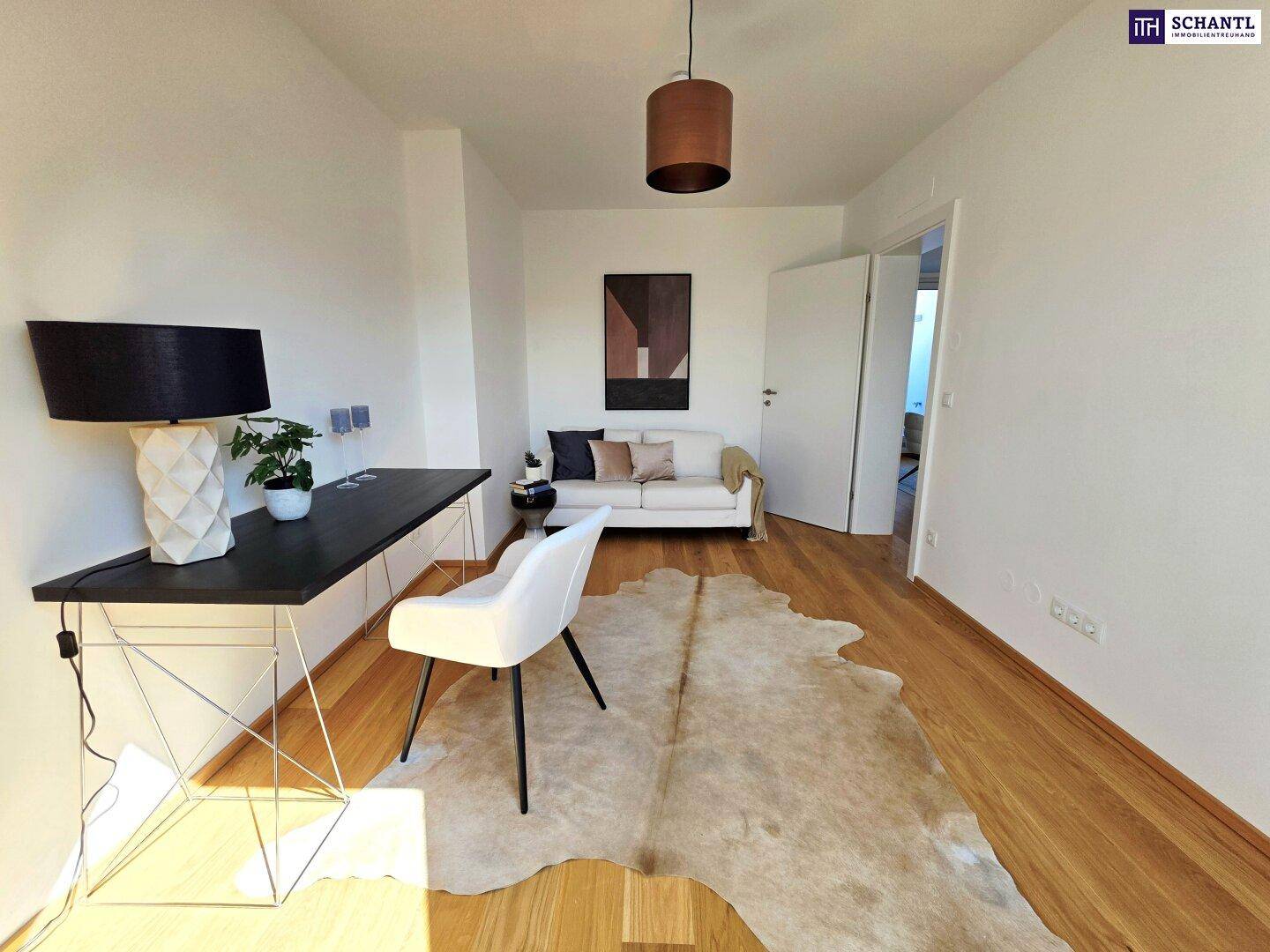 Modern eingerichtetes Arbeitszimmer mit Holzboden, weißer Couch und minimalistischem Schreibtisch.