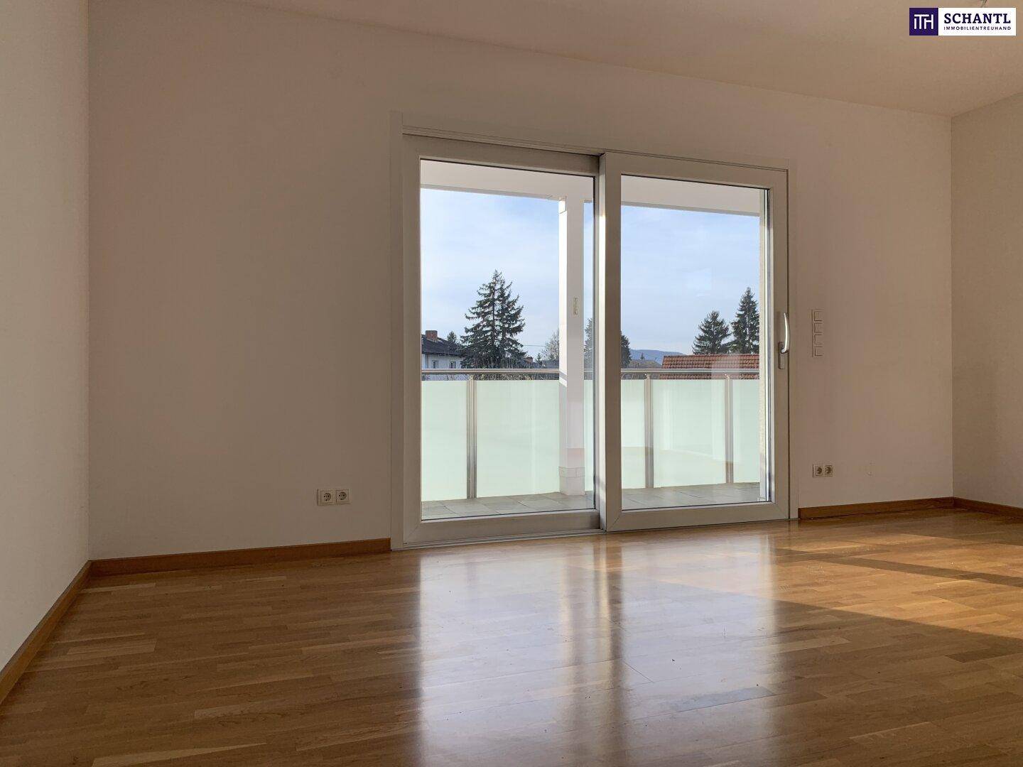 Heller Wohnbereich mit Holzboden und Zugang zu einem Balkon mit Glasbrüstung.