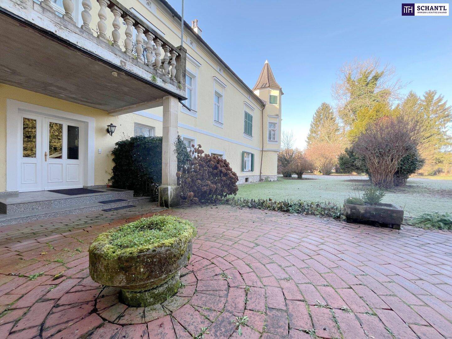 Eingangsbereich des Anwesens mit gepflastertem Vorplatz, historischem Balkon und einem steinernen Pflanzgefäß.
