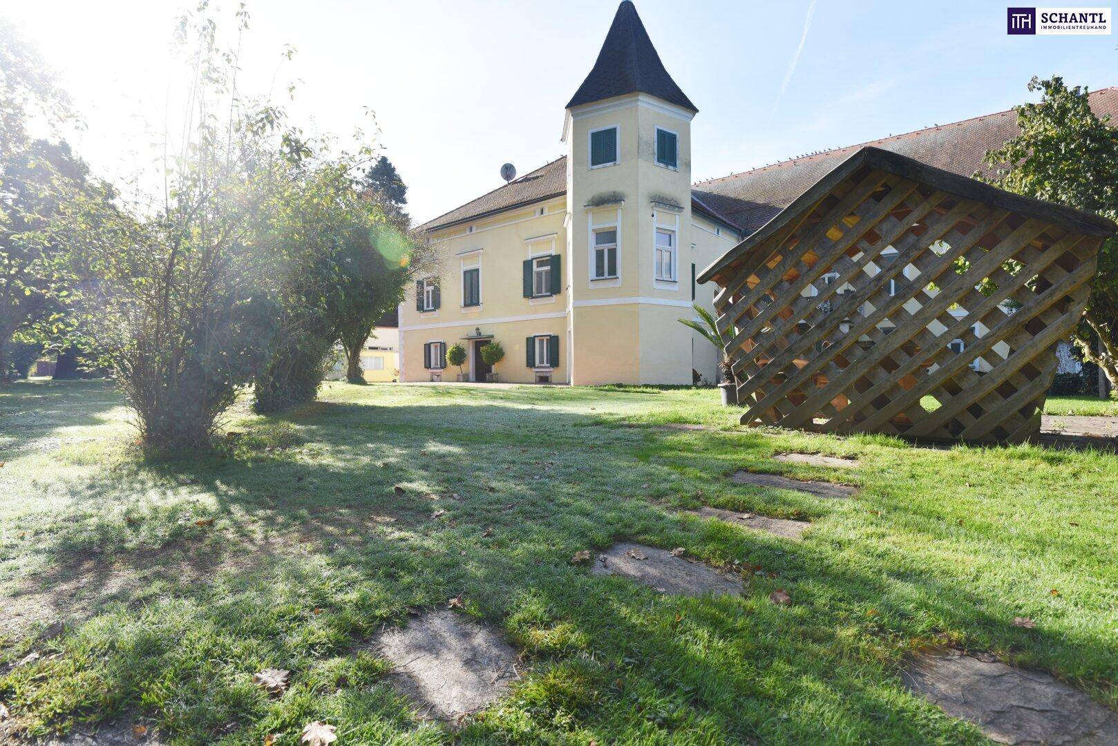 Sonnige Ansicht des Gartens mit einem dekorativen Holzgitter und dem historischen Gebäude im Hintergrund.