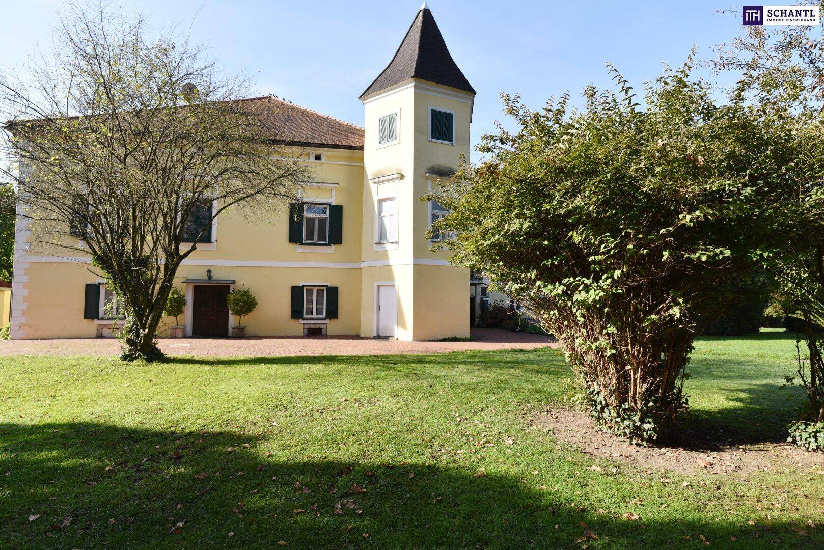 Weitläufiger Gartenbereich mit gepflegtem Rasen und altem Baumbestand vor dem historischen Gebäude.