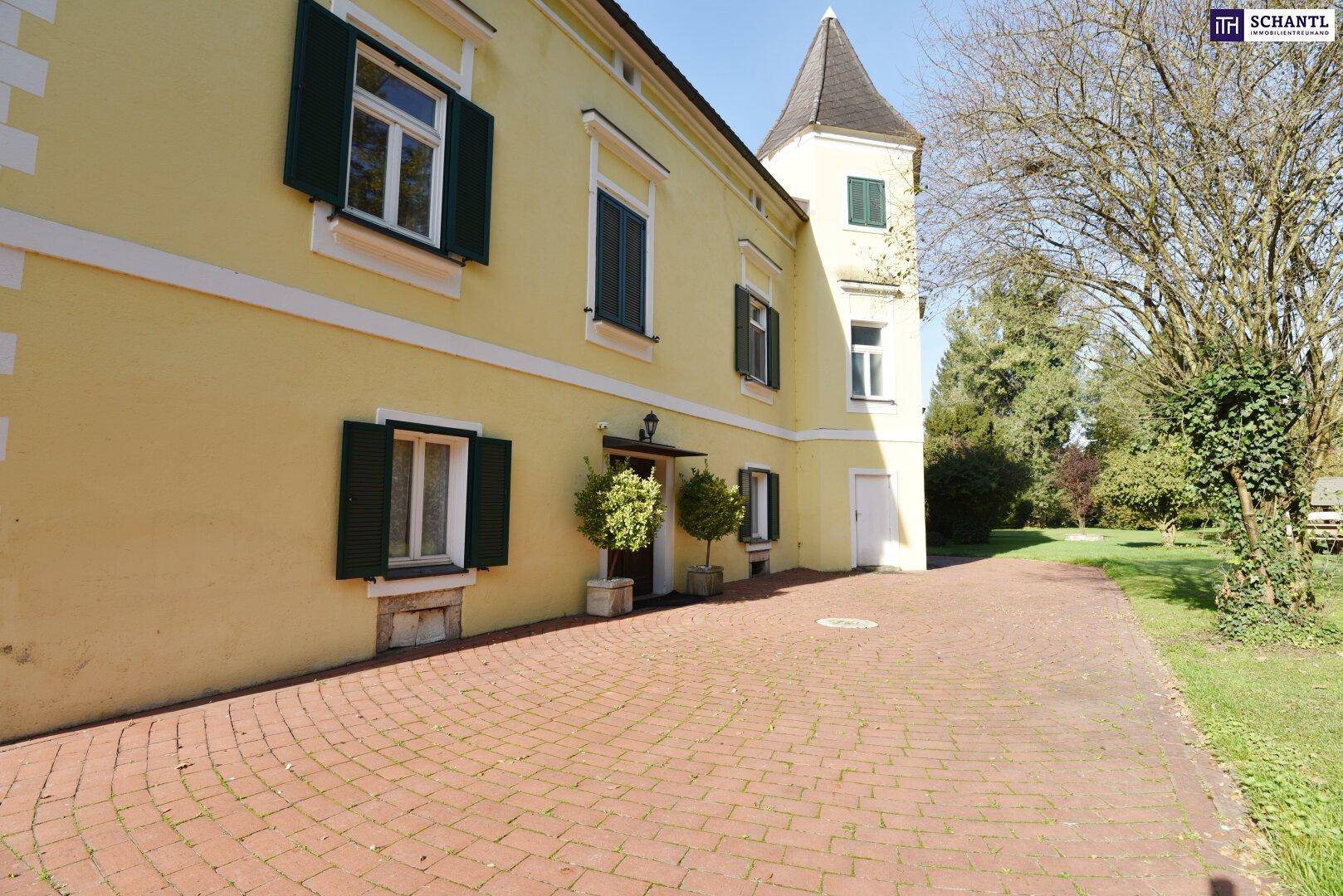 Ansicht der Gebäudefassade mit gelbem Putz, grünen Fensterläden und einem gepflasterten Zufahrtsbereich.