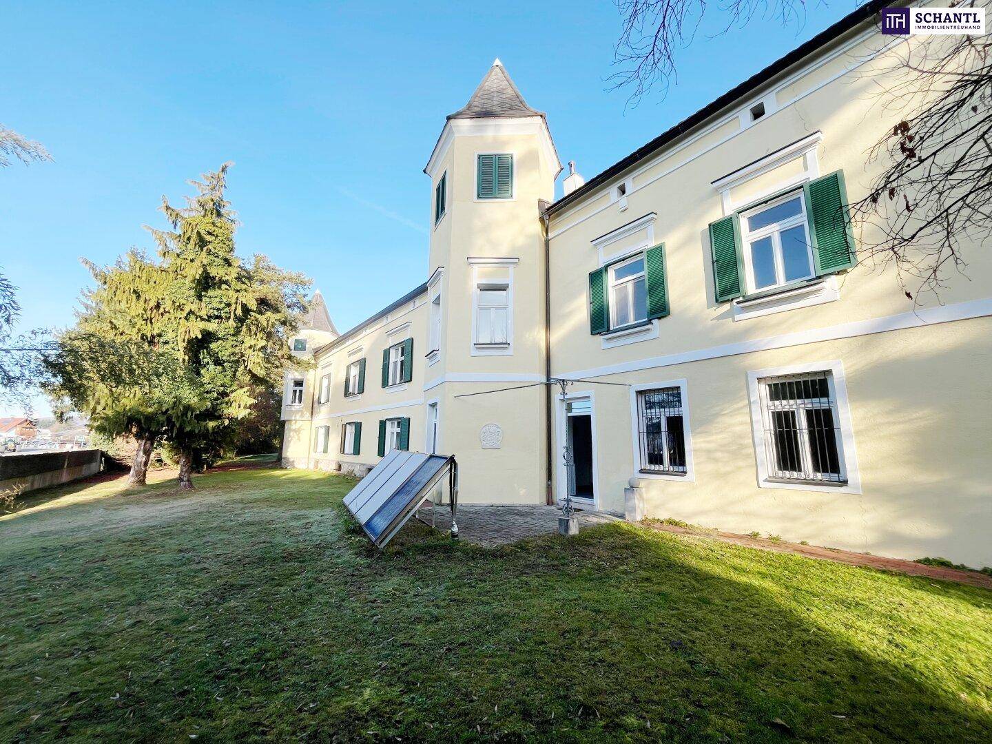 Seitenansicht des historischen Gebäudes mit grünen Fensterläden und einem kleinen Solarpaneel auf dem Rasen.