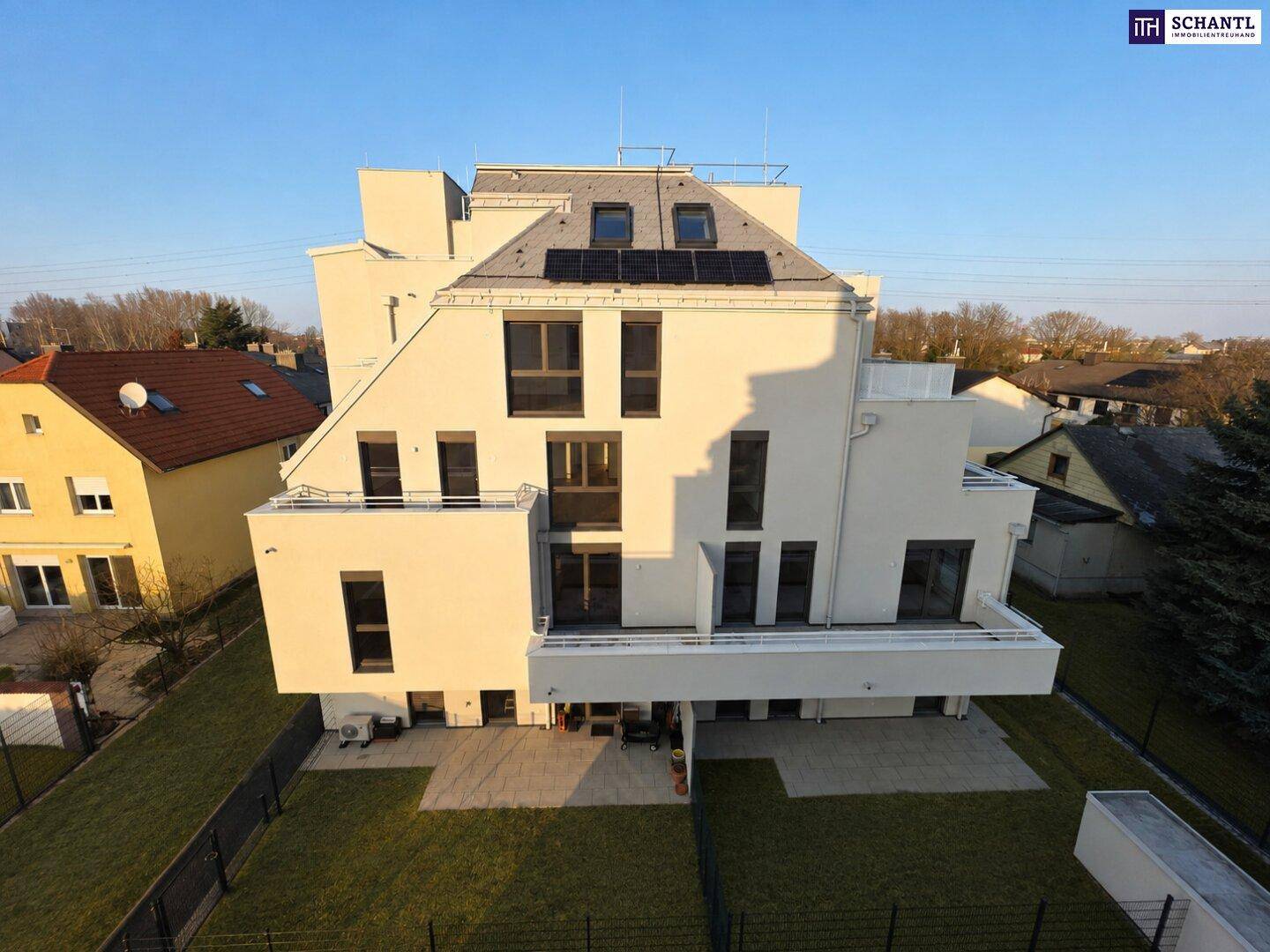 Rückseite eines modernen Wohngebäudes mit einer großzügigen Terrasse und angrenzendem Gartenbereich.