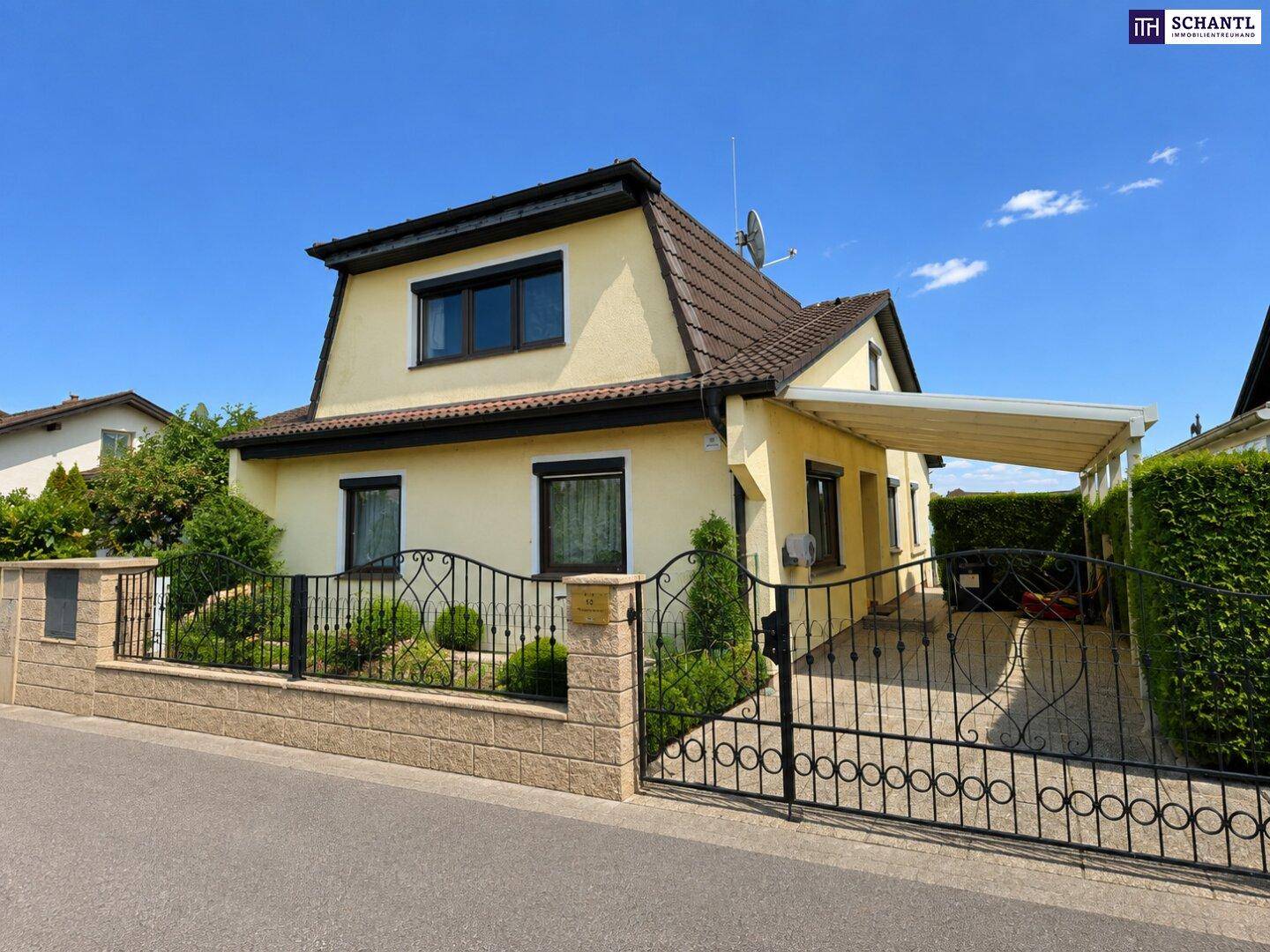 Vorderansicht des Hauses mit schmiedeeisernem Tor, Zaun und überdachtem Stellplatz.
