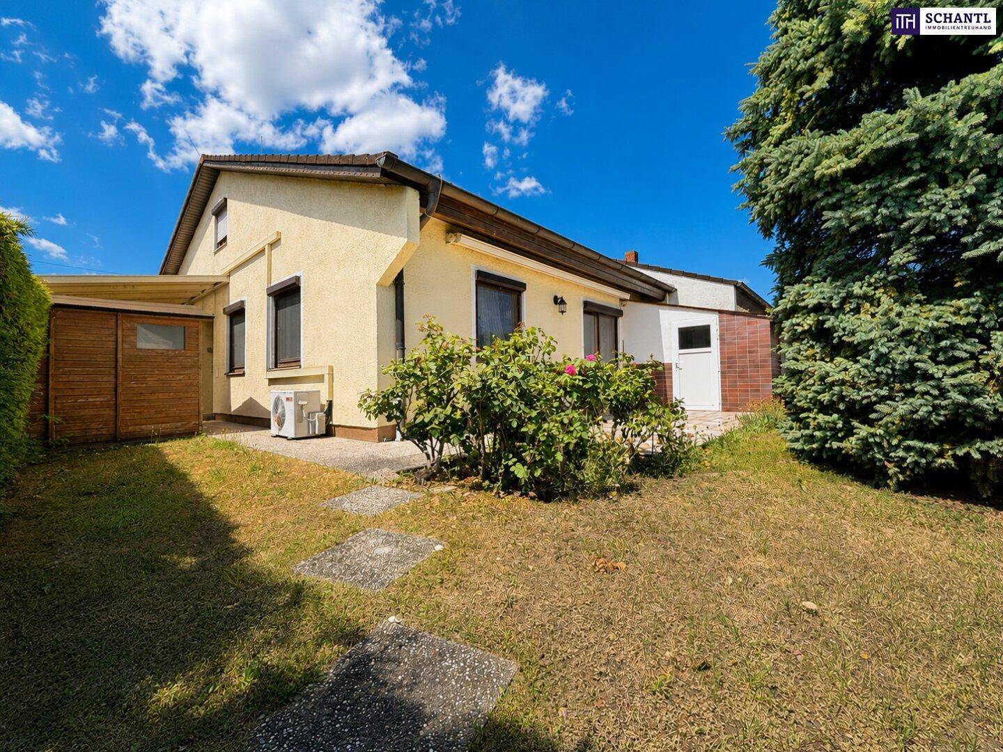 Rückseite des Hauses mit kleiner Rasenfläche und Sträuchern unter blauem Himmel.