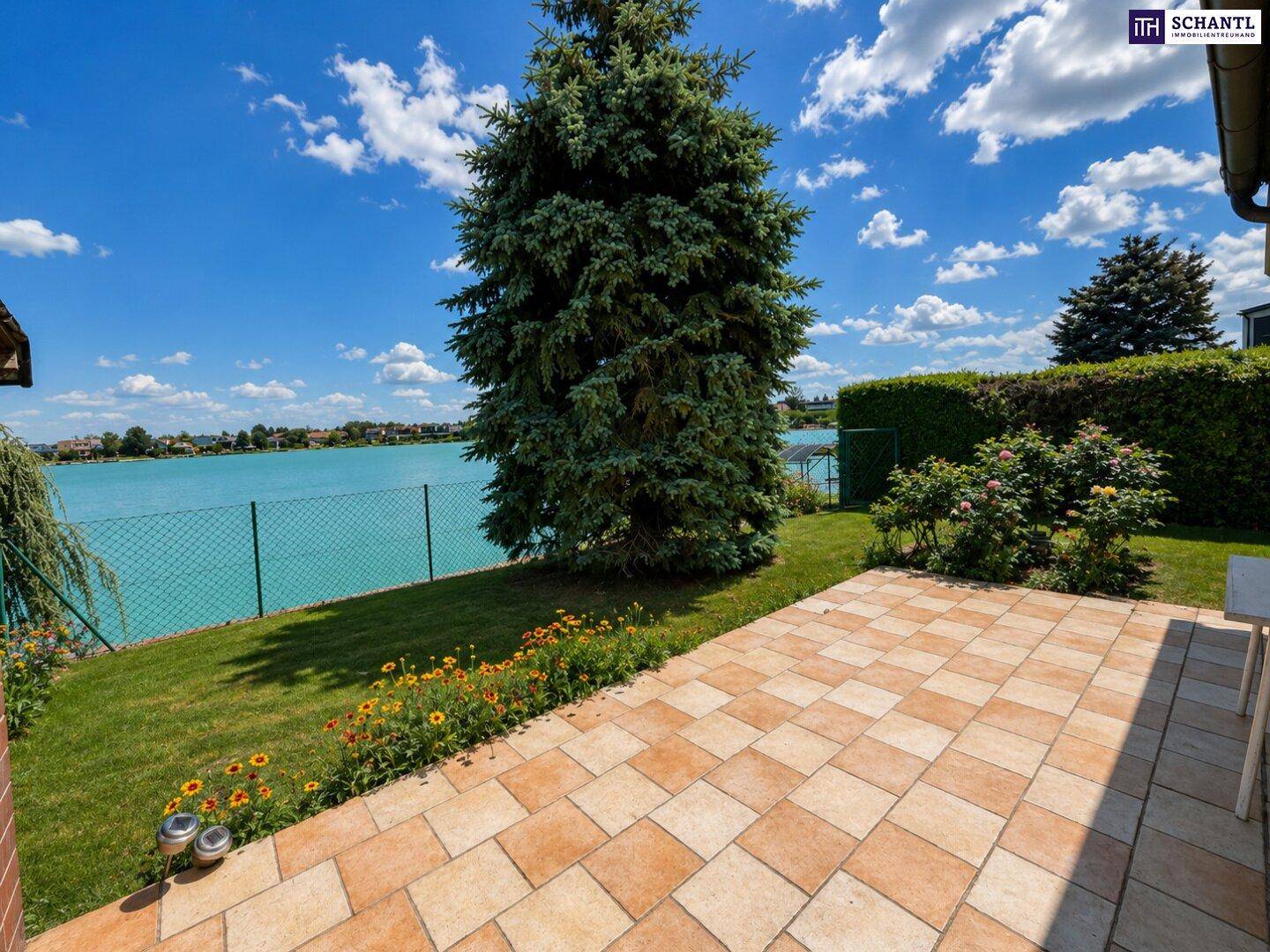 Gemütliche Terrasse mit Rasenfläche und großem Baum, bietet einen schönen Blick auf den See.