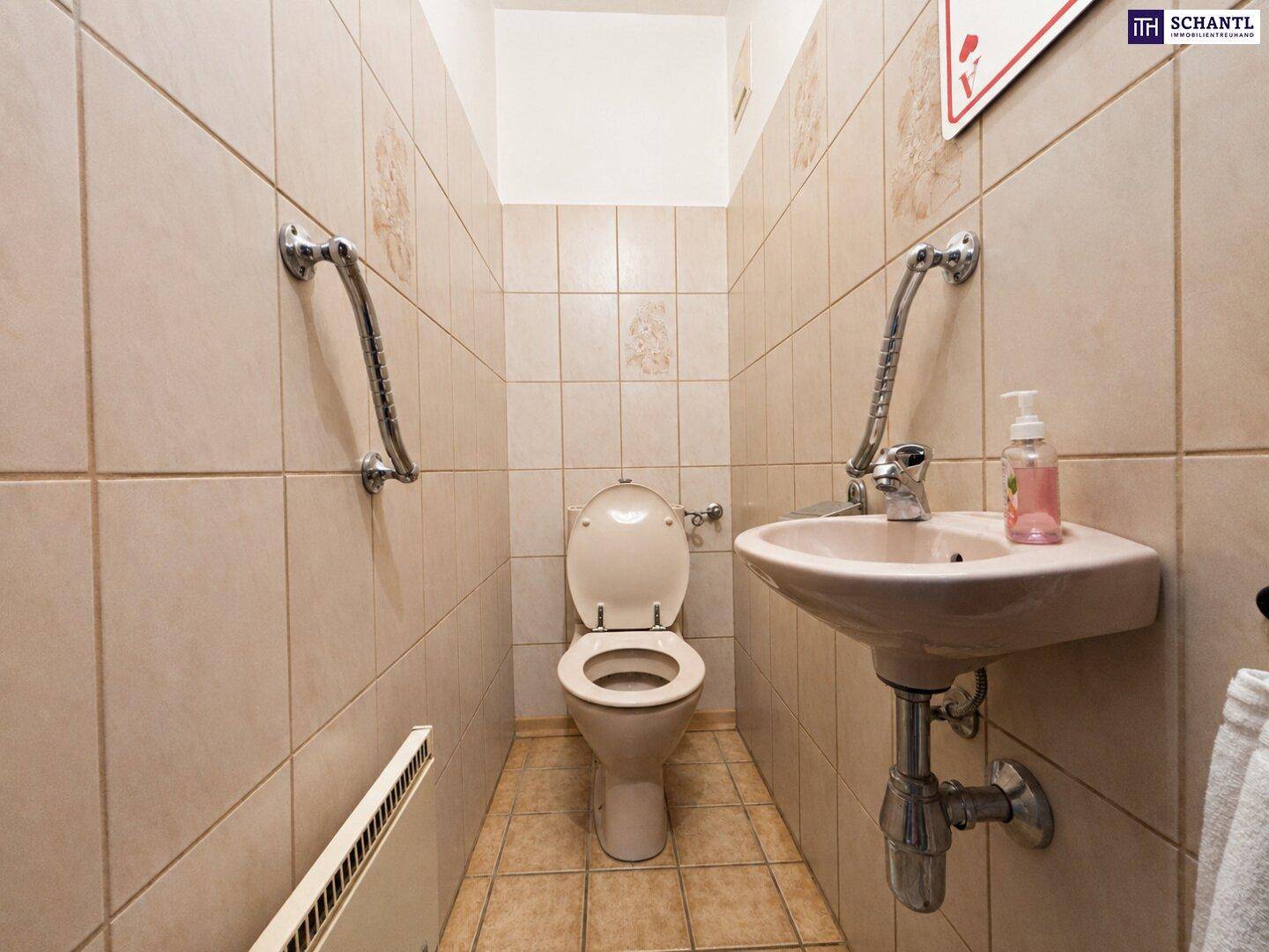 Separates WC mit Toilette, Waschbecken und Haltegriffen für zusätzliche Sicherheit.