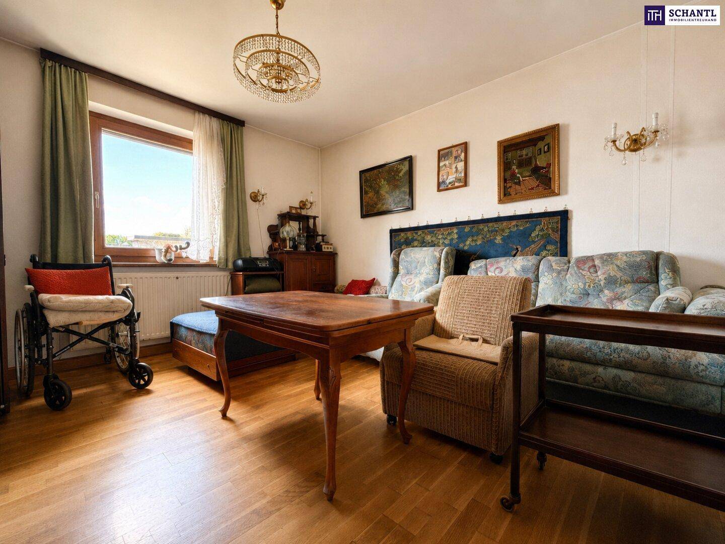 Helles Schlafzimmer mit Parkettboden, großem Fenster und traditionellen Möbeln, inklusive Rollstuhl.
