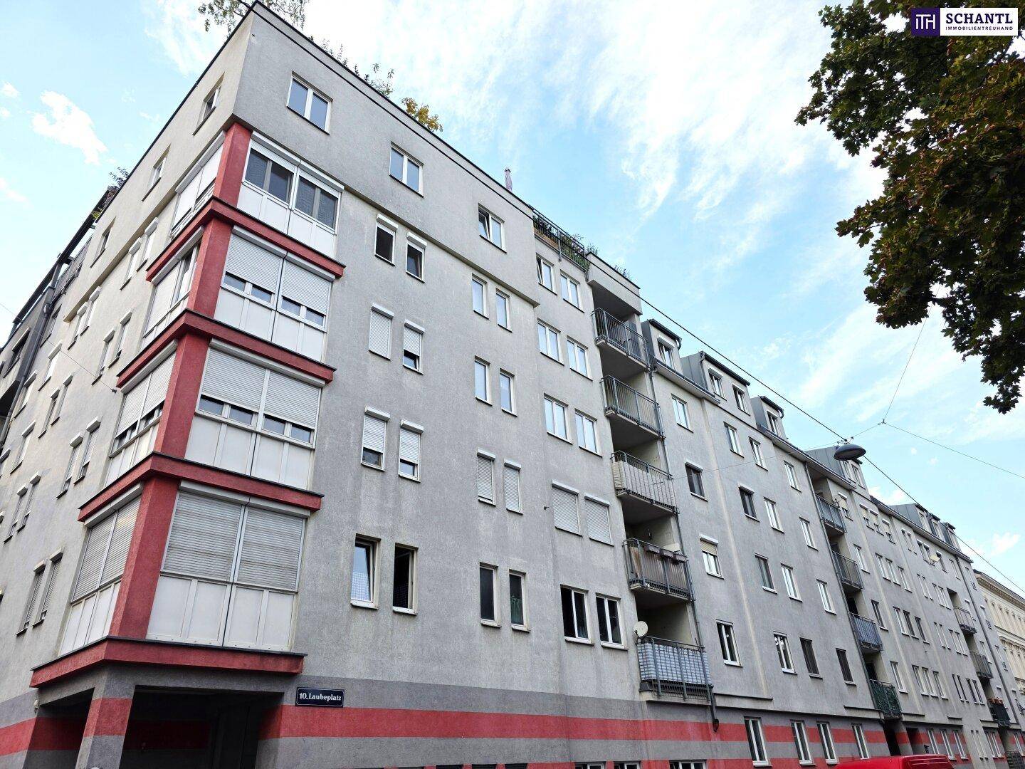 Mehrstöckiges Wohngebäude mit grauer Fassade, roten Akzenten und zahlreichen Fenstern.