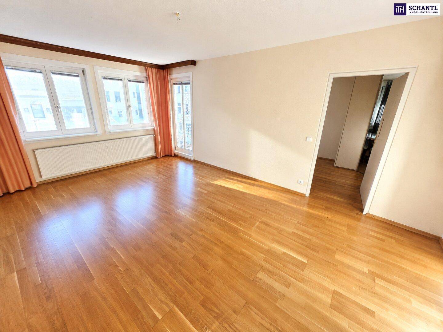 Geräumiges Wohnzimmer mit hellem Parkettboden, großen Fenstern und Zugang zum Balkon.