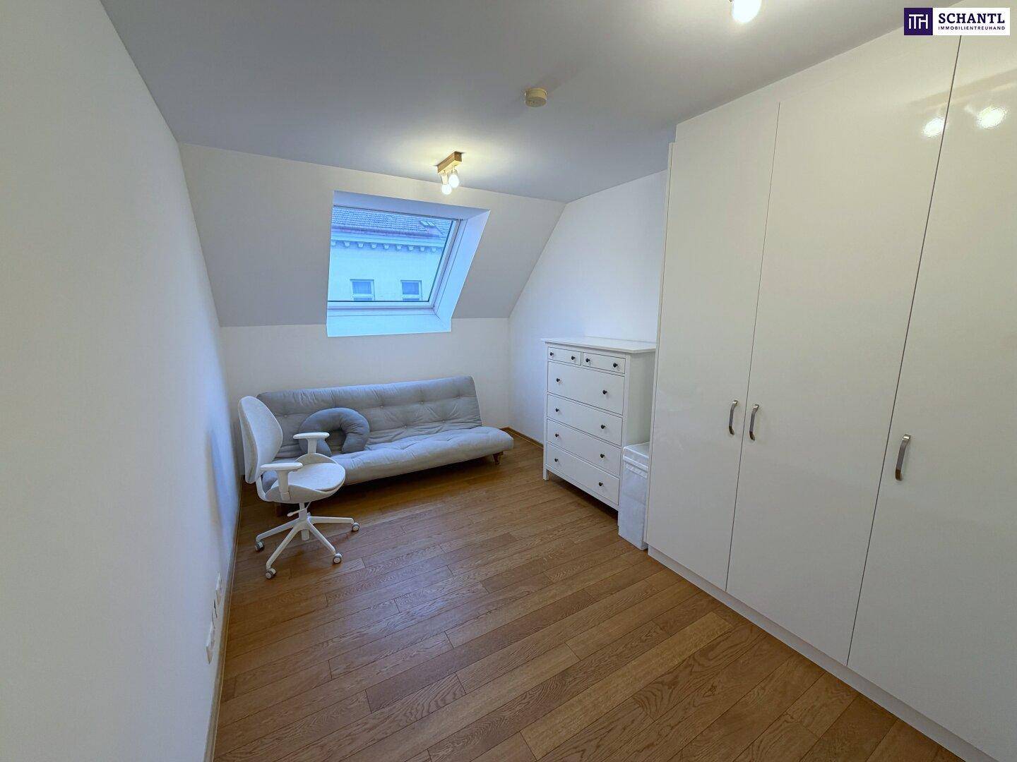 Geräumiges Zimmer mit Dachfenster, Holzboden und weißem Kleiderschrank unter Dachschräge.