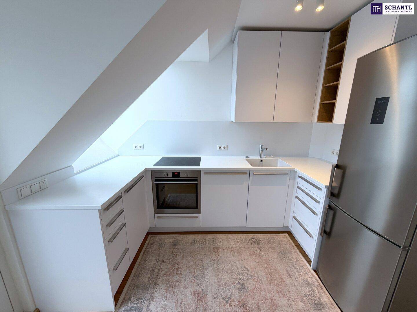 Moderne Einbauküche in Weiß mit Dachschräge, Induktionskochfeld, Backofen und Kühlschrank.