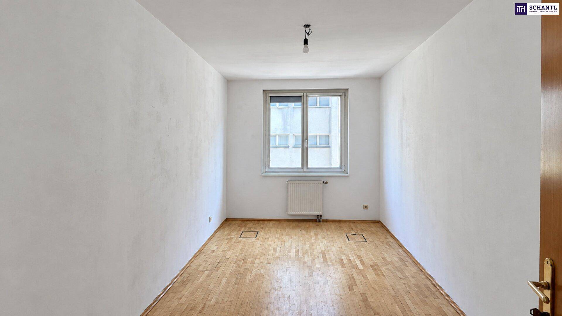Unmöbliertes Schlafzimmer mit Holzboden, weiß gestrichenen Wänden und einem großen Fenster.